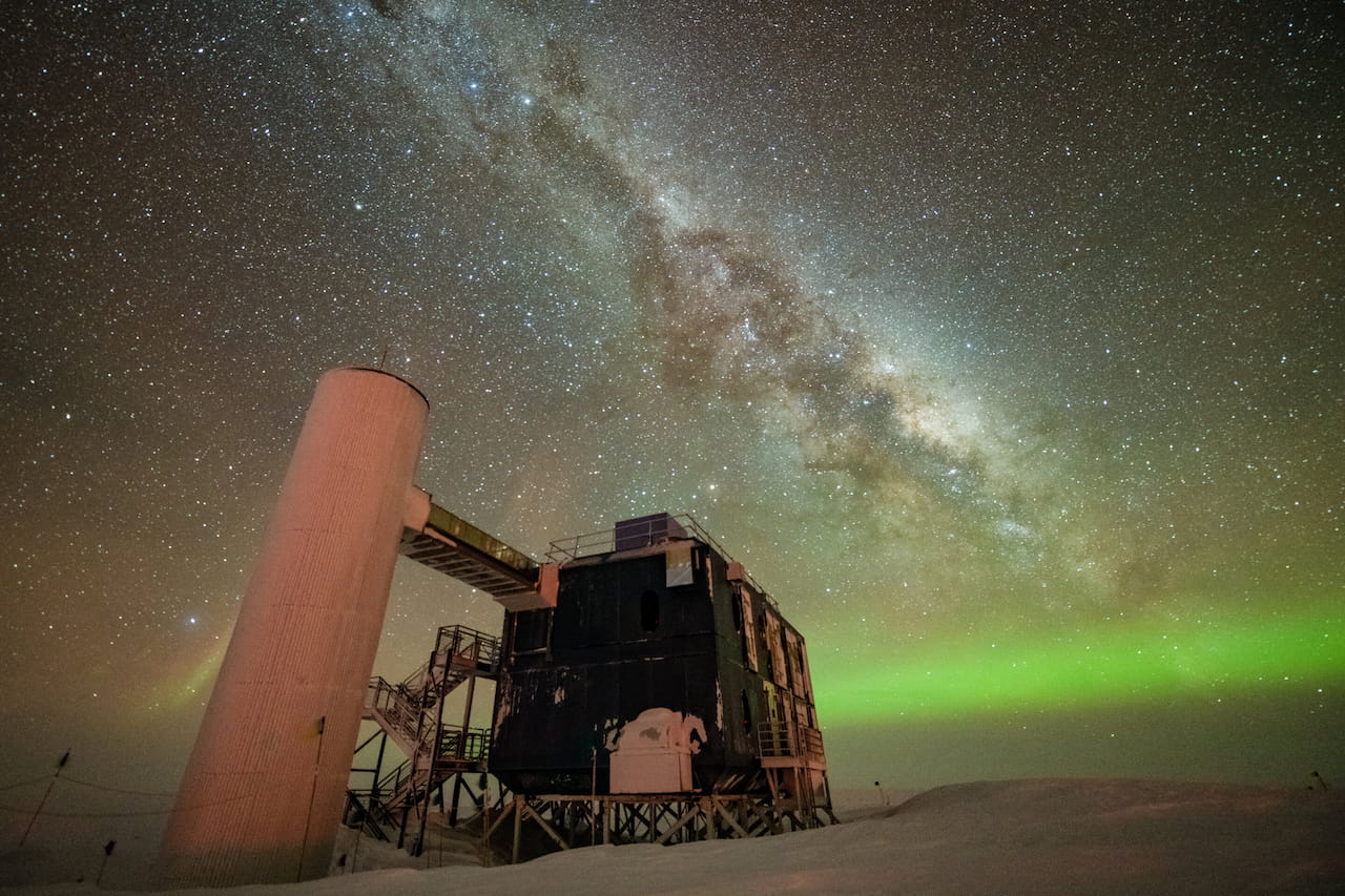 Vista del laboratorio IceCube con un cielo nocturno estrellado que muestra la Vía Láctea y auroras verdes