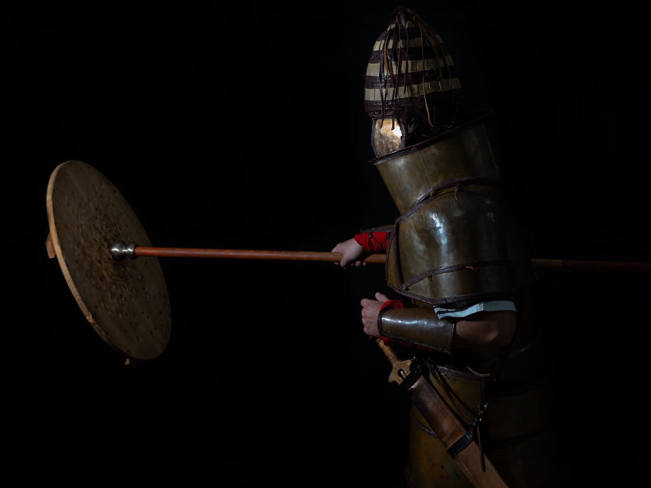 Man wearing replica armor and striking a shield with a spear